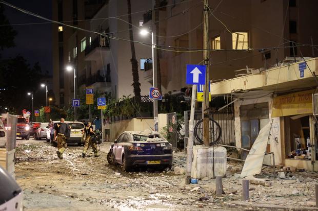 Members of the Israeli security forces walk along a debris-strewn street in Tel Aviv, after it was hit by a rocket fired by Palestinian militants from the Gaza Strip on October 7, 2023. 